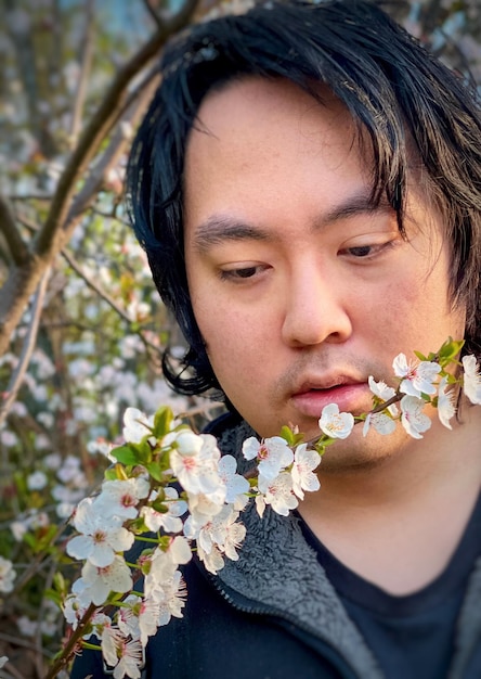 Close-up of young asian man with white cherry plum blossoms against flowering tree