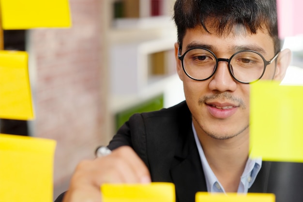 창의적인 아이디어, 사무실 라이프 스타일, 비즈니스 개념의 성공을 브레인 스토밍하는 사무실에서 스티커 메모에 작성하는 젊은 아시아 남자의 닫습니다