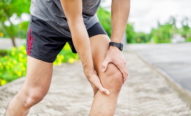 Close up of young asian sports man has pain at muscles and\
joints during outdoor exercise, over trainning or running and sport\
injuty concept