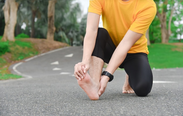 Close up of young Asian sports man has pain at muscles and joints during outdoor exercise, over trainning or running and sport injuty concept