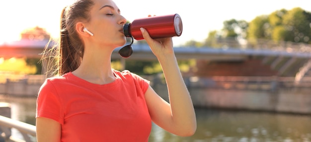 Primo piano di una giovane sportiva stanca attraente all'aperto, acqua potabile da una bottiglia.