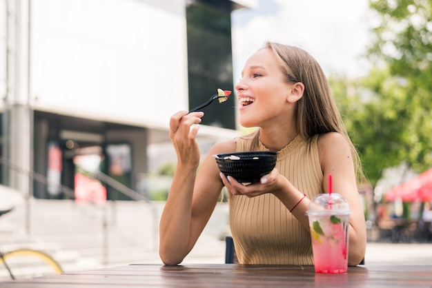 Primo piano di una giovane donna attraente che mangia insalata al caffè di strada?