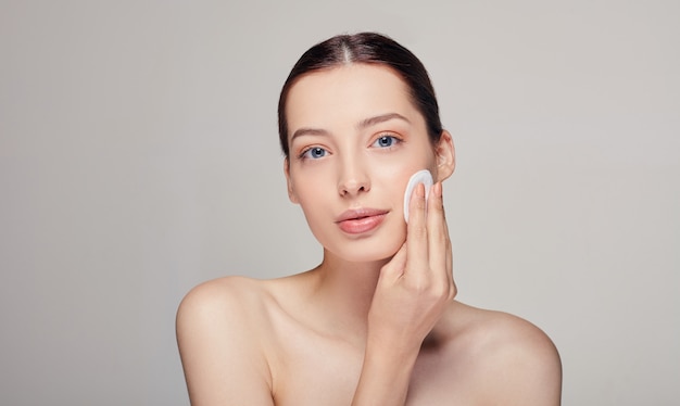 Close-up young beautiful tender calm woman with a cotton pad in in her right hand looks straight with blue eyes on the