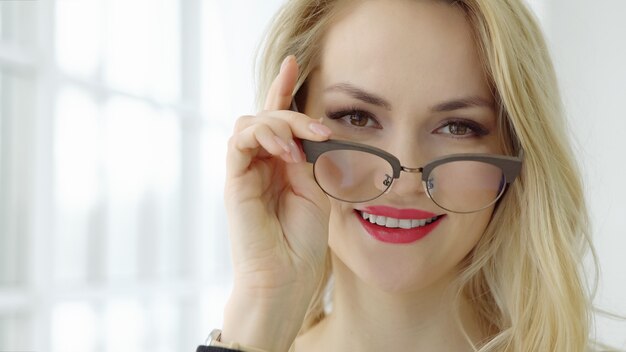 Close up of a young beautiful woman with glasses at the window and looking at camera, selective focus