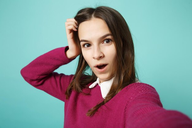 Close up young brunette woman girl in casual clothes posing doing selfie shot on mobile phone isolated on blue background studio portrait. People sincere emotions lifestyle concept. Mock up copy space