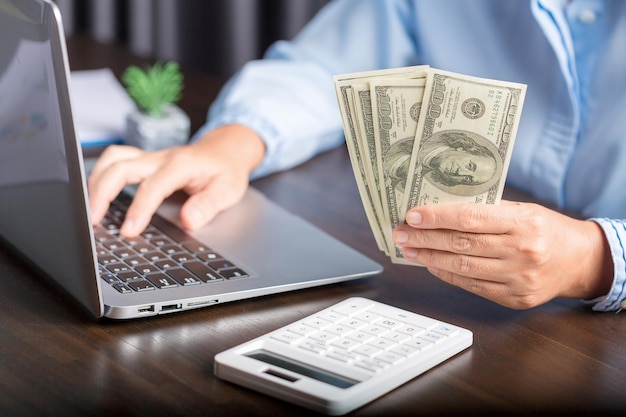 Close up young business woman using counting cash money one hundred dollar bills checking financial documents sitting at table