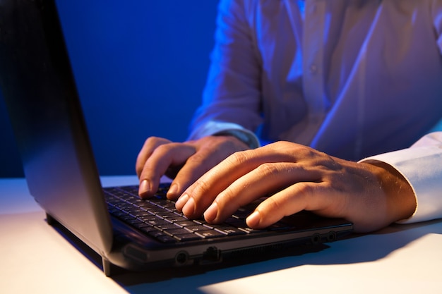 Close up of young businessman working on a laptop on dark background