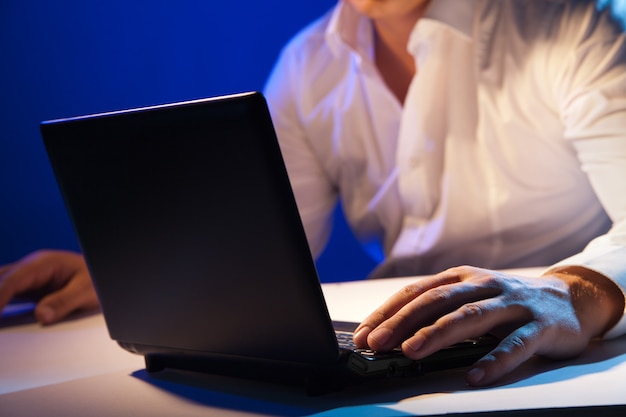 Close up of young businessman working on a laptop on dark background