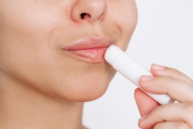 Close up of a young caucasian attractive woman applying a hygienic lipstick on her lips