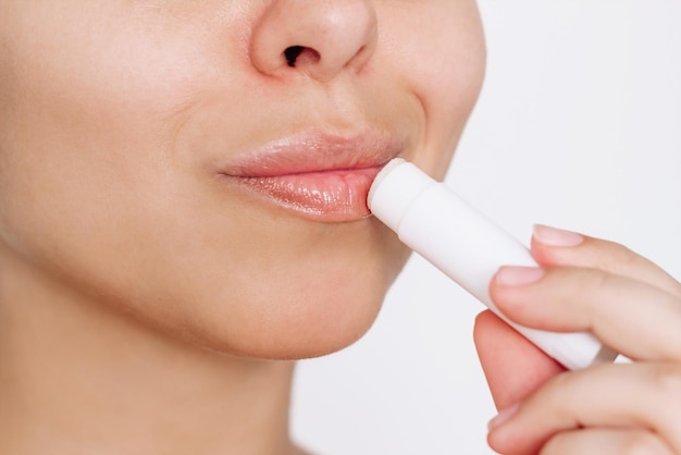 Photo close up of a young caucasian attractive woman applying a hygienic lipstick on her lips