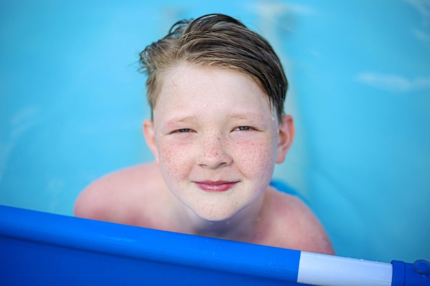 Close-up young child with freckles holding handrails smiling in pool with clean warm water on sun