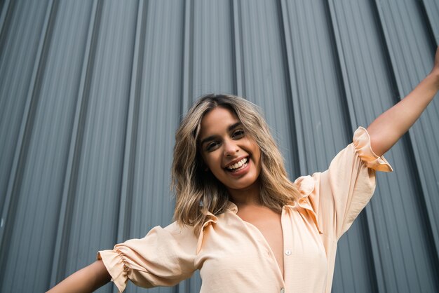 Close-up of young confident woman smiling and celebrating while standing outdoors on the street. Urban concept.