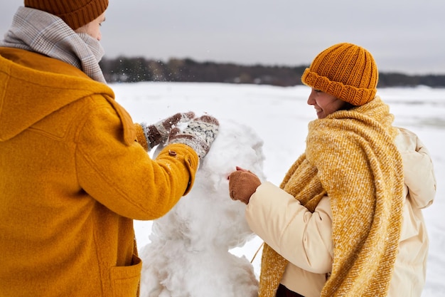 屋外で冬の楽しみを楽しみながら一緒に雪だるまを作る若いカップルのクローズ アップ