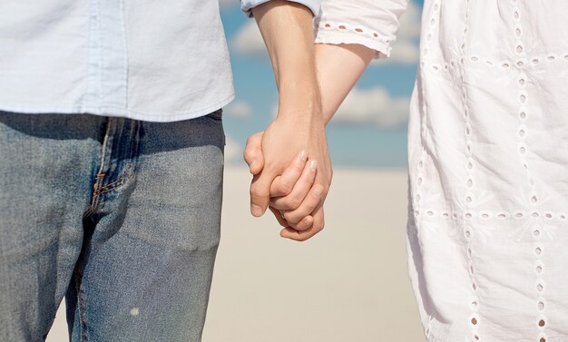 Photo close-up of a young couple enjoying the sunset in the dunes holding hands. romantic traveler walks through the desert. adventure travel lifestyle concept