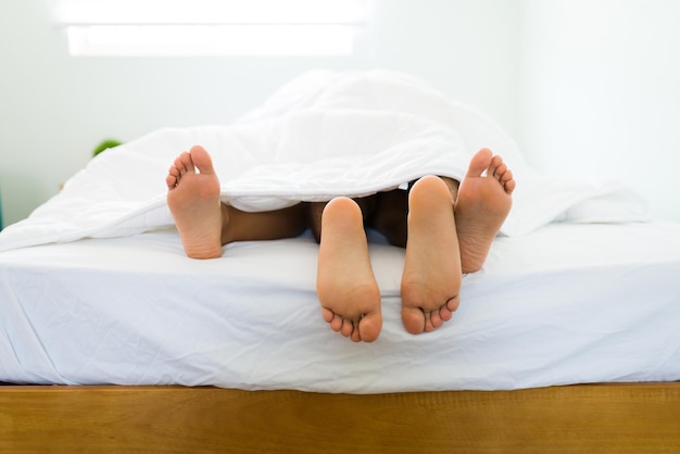 Premium Photo Close up of a young couples feet lying in bed under the covers