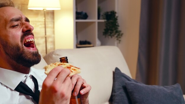 Photo close up of young entrepreneur laughing while watching tv and drinking beer.