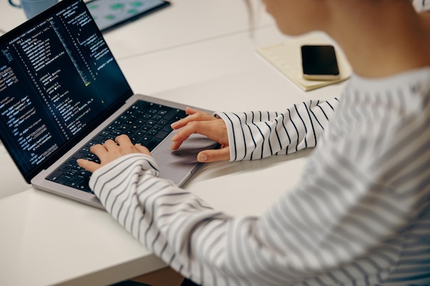 コワーキングで座ってラップトップでコードを書いている若い女性コンピュータープログラマのクローズアップ