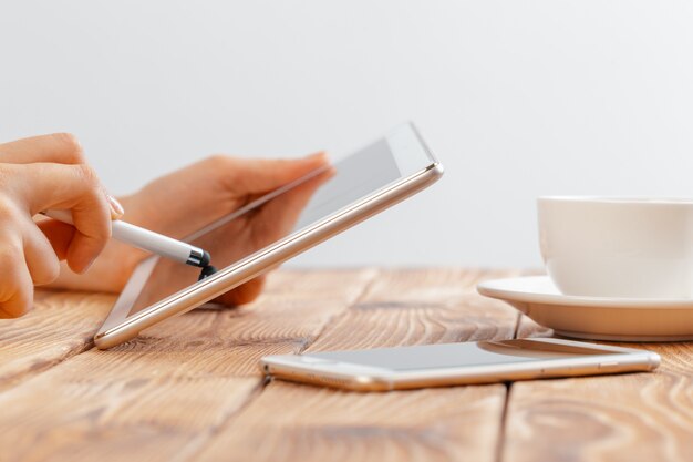 Primo piano di giovani mani femminili che tengono compressa digitale e che bevono il macchiato di mattina.