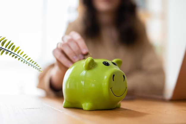 Close up young female putting coin in piggy bank. Woman saving money for household payments