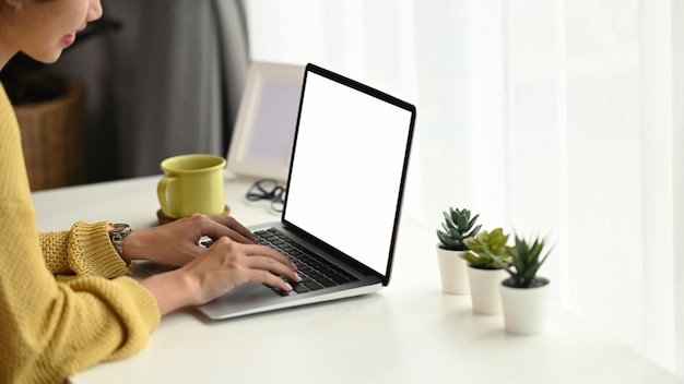 Close up of young female typing on laptop while sitting in front of blank screen laptop