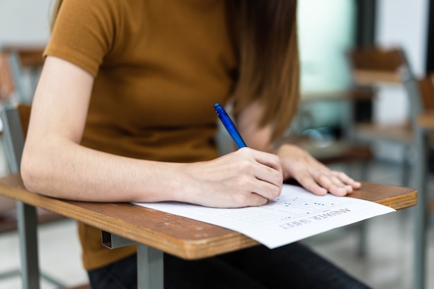 Primo piano di giovani studentesse universitarie si concentrano sul fare l'esame in classe. una studentessa scrive la risposta degli esami sul foglio delle risposte in classe.