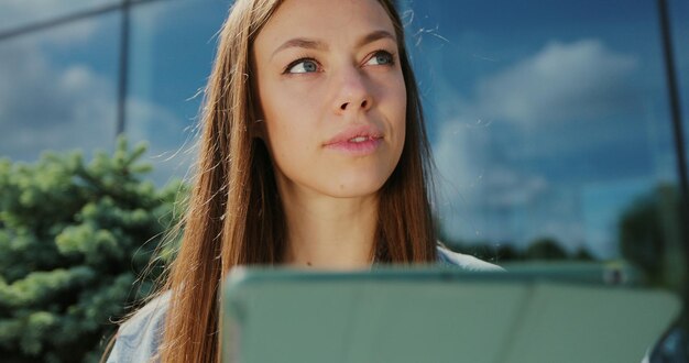 Photo close up of young girl using tablet computer outdoors in the street while sitting on the bench pretty female tourist strolling and looking at screen browsing internet chatting