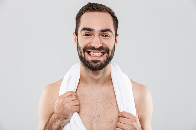 Close up of a young handsome bearded shirtless man standing isolated over white, holding towel over his shoulders