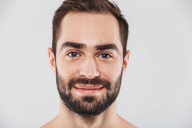 Foto primo piano di un giovane uomo barbuto bello a torso nudo in piedi isolato su bianco