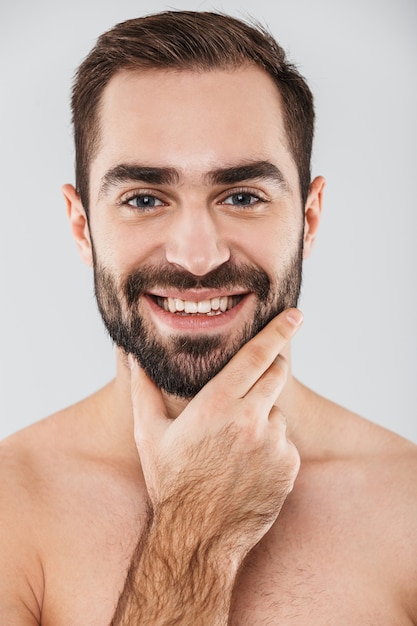 Close up of a young handsome bearded shirtless man standing isolated over white