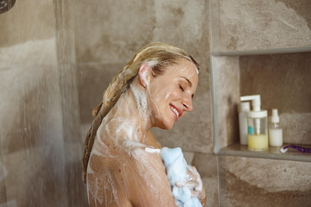 Close up of young happy pretty woman smiling and washing herself with soap in shower