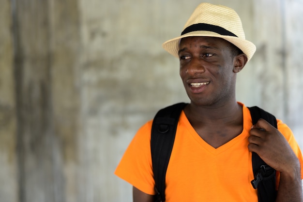 Close up of young happy tourist man smiling and thinking against concrete wall in the sky train station of Bangkok Thailand