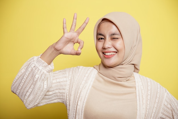 행복 한 젊은 hijab 여성을 닫고 노란색 배경에 고립 된 확인 표시를 보여줍니다.
