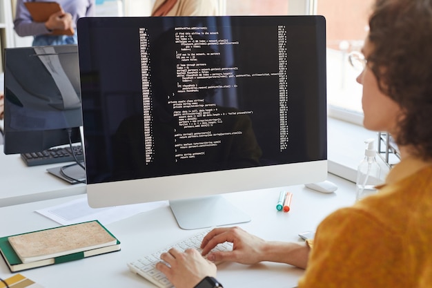 Close up of young IT developer writing code on computer screen while working in software production studio, copy space