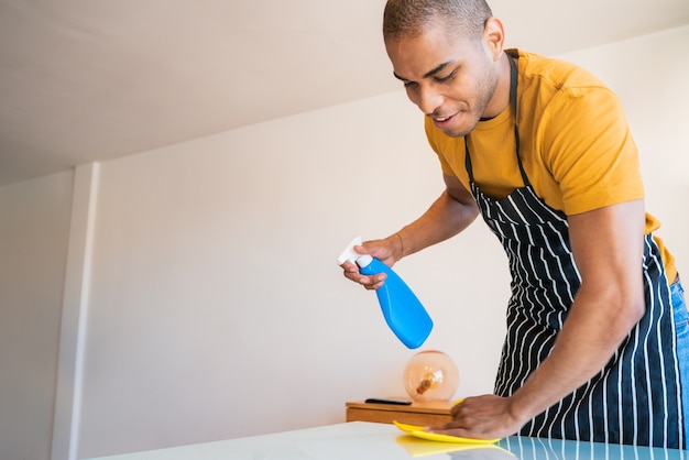 Close up of young latin man cleaning stains off the table at home. Housekeeping and cleaning concept.