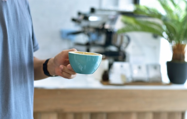 Chiuda in su delle mani maschii giovani che tengono una tazza di caffè