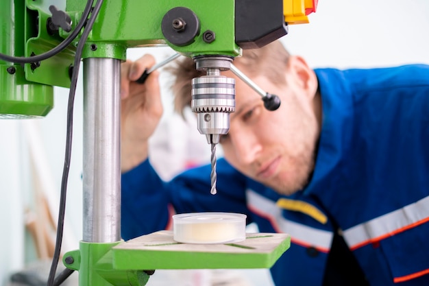 Close up young male worker using a drill machine on the factory