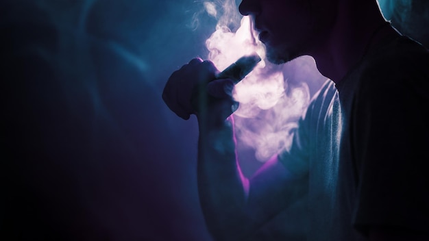 Close up of a young man exhaling a cloud of steam or smoke using an electronic cigarette Mechanical vaping mod