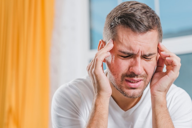 Photo close-up of a young man grimacing in pain touching his head with fingers