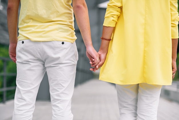 Close up young man and his girlfriend in casual clothes holds the hands to each other. View from back.