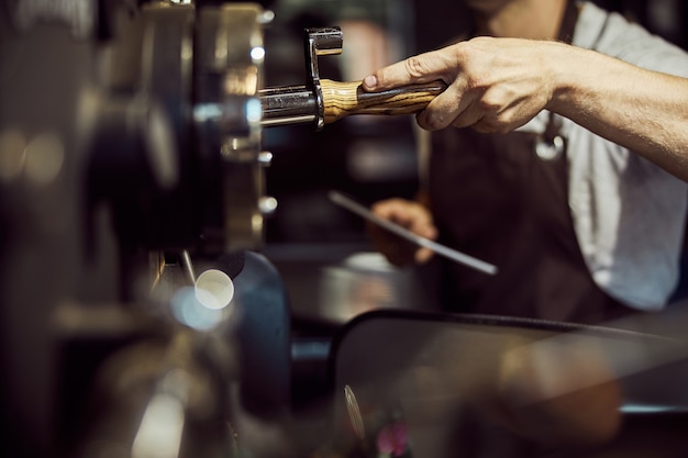 Close up of young man holding tablet computer while using professional equipment for roasting coffee beans