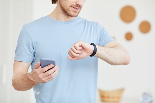 Foto primo piano del giovane che guarda il suo orologio e controlla il suo tempo con il telefono cellulare