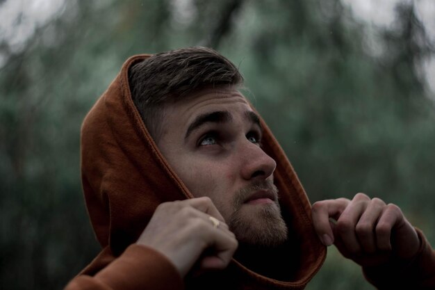 Photo close-up of young man looking up while standing against trees