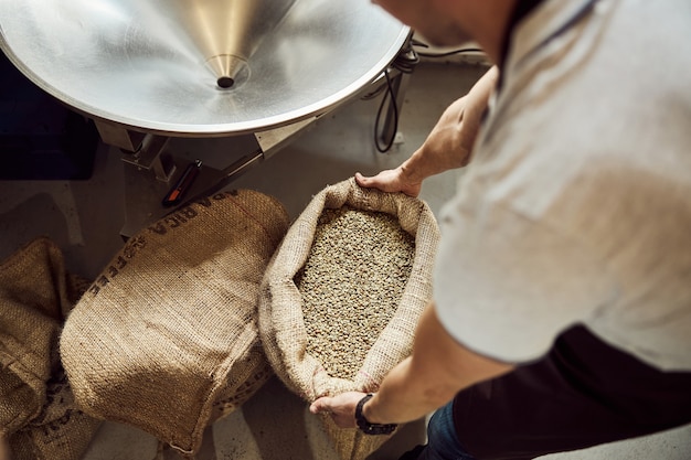 Close up of young man's hands holding open bag with unroasted coffee beans