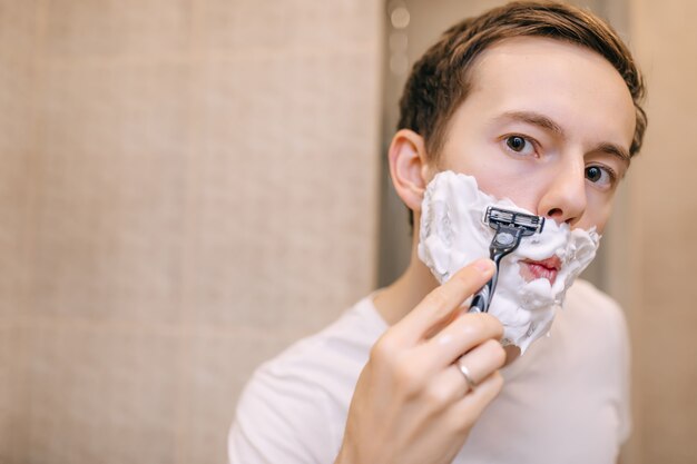 Close up of a young man shaving using a razor