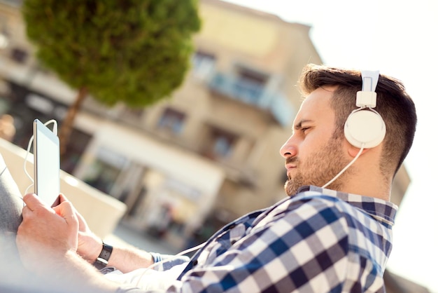 Close up of a young man sitting outdoors listening to music