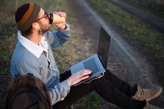 脚にラップトップと手にコーヒーのカップで座っている若い男のクローズアップ