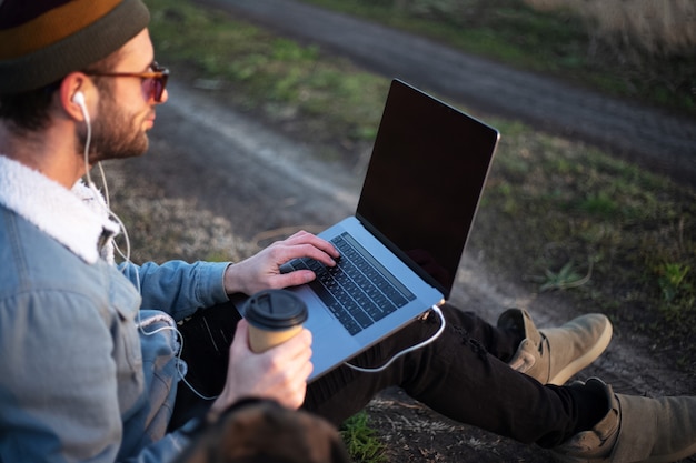 Close up of young man sitting with laptop on legs and cup of coffee in hand