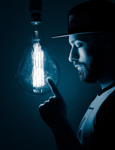close-up of young man standing in front of illuminated light bulb in darkroom