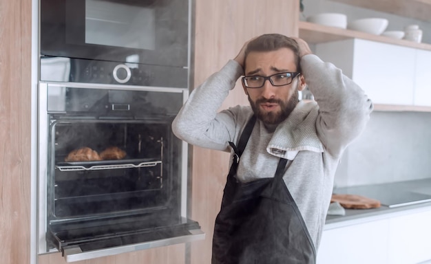 Photo close up a young man takes out of the oven tray of croissants