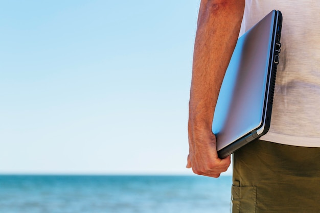 Photo close up young man on vacation holding closed laptop at the beach